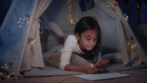 Pretty Girl in Cute Decorative Tent with Lighting Browsing Internet at Home in Evening alt