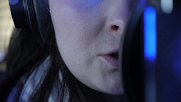 Young professional female singer in headphones singing in recording studio alt