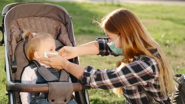 European Mother Is Putting a Protective Mask on a Daughter's Face in a Stroller alt