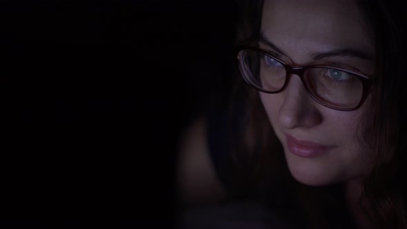 The Girl in Glasses Uses a Laptop Lying on the Bed at Night. Isolated Light alt