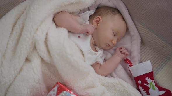 Zoom in to Cute Little Baby Girl Lying on Cozy Bed with Christmas Stocking and New Year Present alt