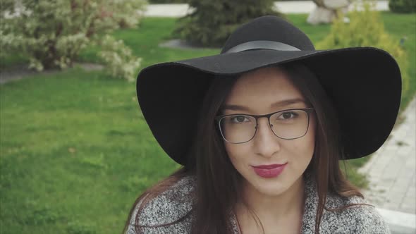 Close Up Portrait of Pretty Smiling Woman in Black Hat and Glasses in the Park alt