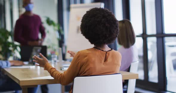 Diverse business people wearing masks sitting listening to a presentation in office alt