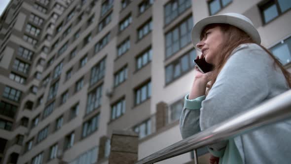 Brunette Woman in Hat Talking on the Phone Standing Near the Building Overweight Woman