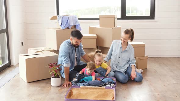 Bearded Darkhaired Man and His Wife Unpack Suitcase Sit on Floor in New Light House alt