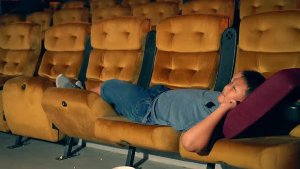 A Boy Laying Down on Armchair in Cinema alt