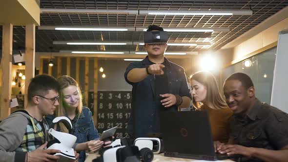 People Working at Laptop Tablet While their Young Male Cowoker in Virtual Reality Glasses alt