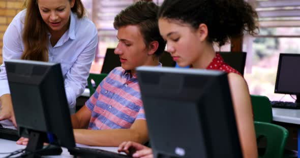 Teacher assisting students in computer class alt