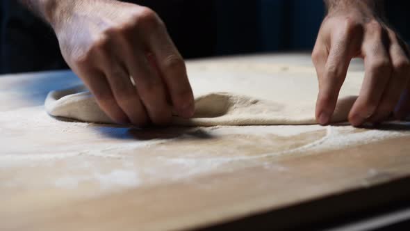 A close-up of a skilled chef's hands put pizza dough on the wooden counter, shallowing it and set it alt