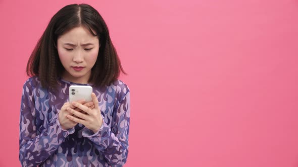 Displeased Asian woman typing on mobile alt