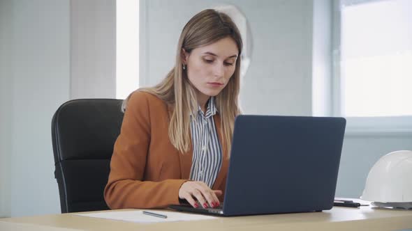Woman Using Laptop and Making Notes on Document in Office
