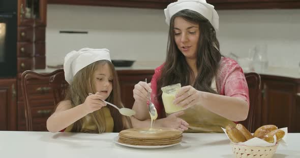 Caucasian Mother and Daughter Applying Condensed Milk on Baked Cake alt