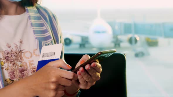Close-up, Woman in Mask, with Passports and Tickets, Uses Mobile, Sitting in Front of Panoramic alt