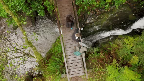 Overhead View Group of Tourists Walking Cinematic Wet Wooden Bridge Over River alt