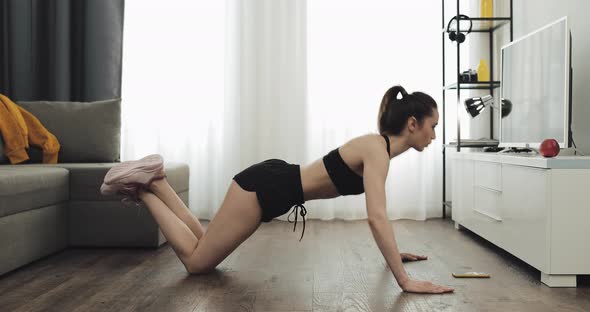 Young Fitness Woman in Athletic Workout Clothes Doing Ush-ups Exercise While Using a Stopwatch on