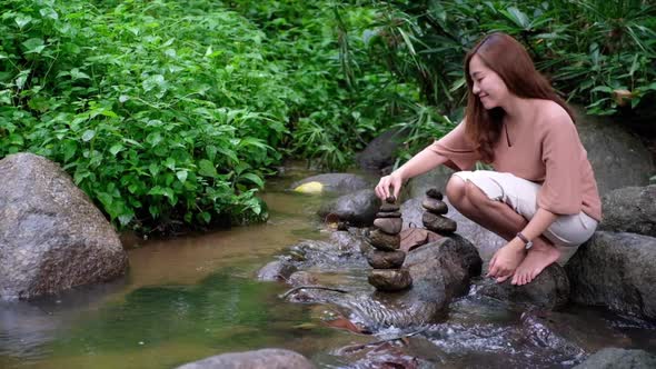 Slow motion of a young asian woman relaxing and stacking stone by the waterfall