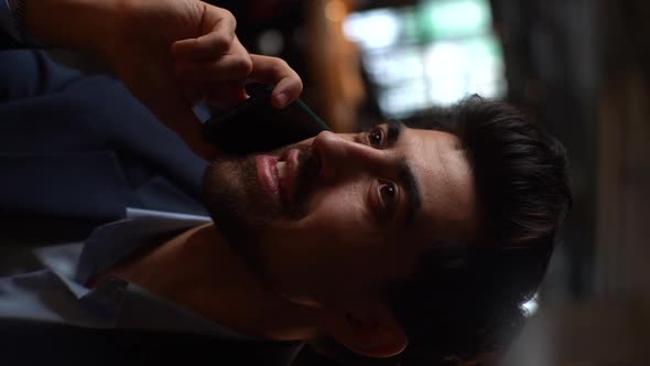 Closeup Vertical Shot of Cheerful Bearded Young Businessman Wearing Suit Talking on Mobile Phone alt