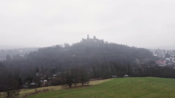 Braunfels Castle behind a green field on a cold and foggy winter day. Aerial tracking shot alt