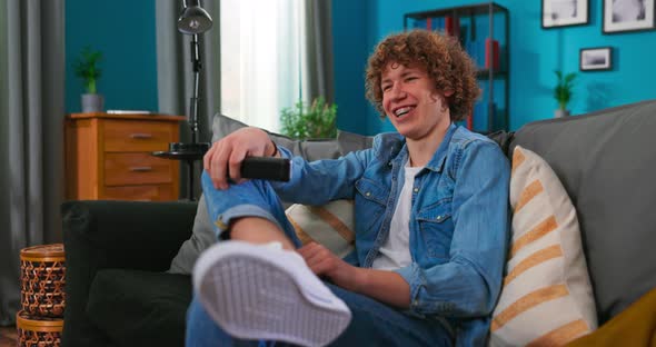 Teenager 20s Boy Sitting on Cozy Sofa and Watching Comedy on TV Laughing with Humorous alt