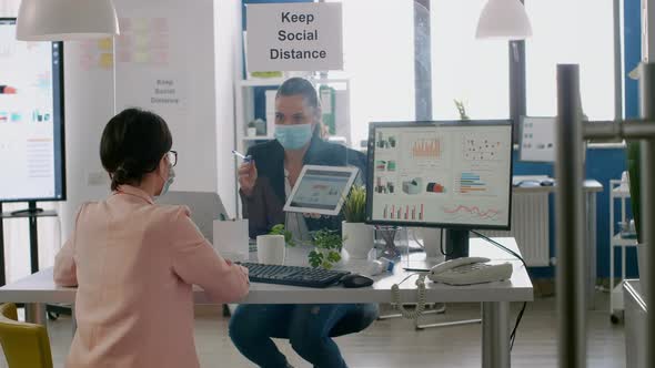 Executive Manager with Face Mask Showing Statistics to Her Collegue alt