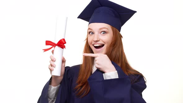 Exciting Caucasian Ginger Graduate Girl in Blue Robe and Square Academical Cap Showing Diploma alt