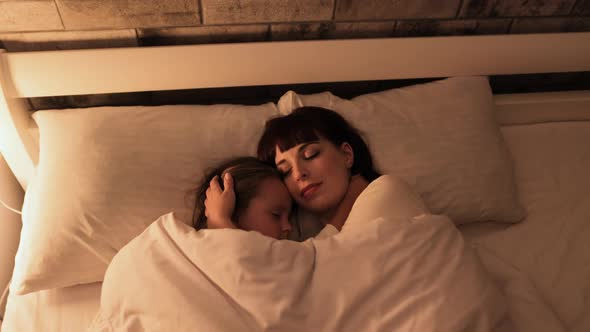 Little Girl Lying on Pillow with Her Pretty Mother Hugging and Sleeping Together in Bed alt