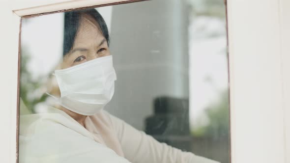 Lonely Asian old woman looking outside the window, Stay home for quarantine. alt