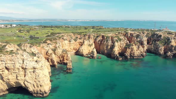 Fly over emerald Atlantic ocean off Lagos. Ponta da Piedade lighthouse overlooking cliffs alt