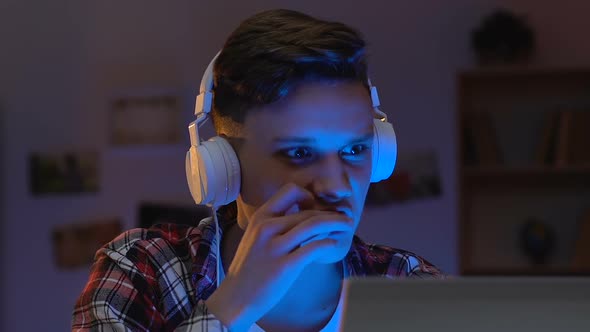 Excited Teen Guy in Headset Watching Video on Laptop at Home, Rooting for Team alt