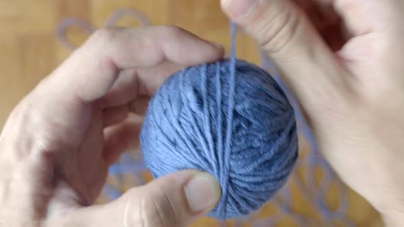 Close up of hand winding ball of blue wool. Blur background. Top view alt