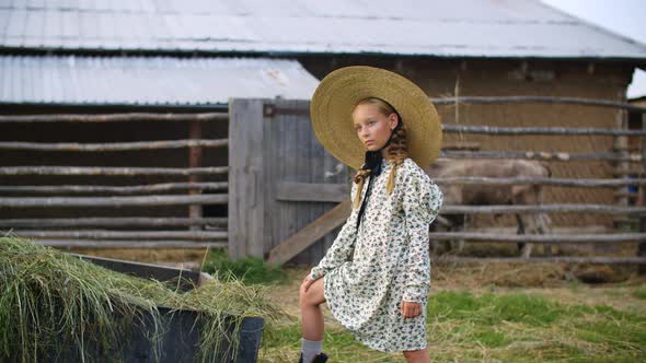 Cute Teen Girl in Dress and Straw Hat Posing on Farm in Countryside