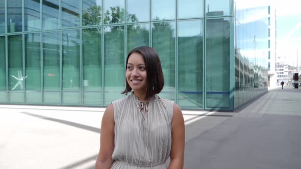 Attractive businesswoman stands smiling in front of the glass facade of a modern office building alt