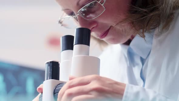 Low Angle Handheld Shot of Mature Female Researcher Looking Through a Microscope alt