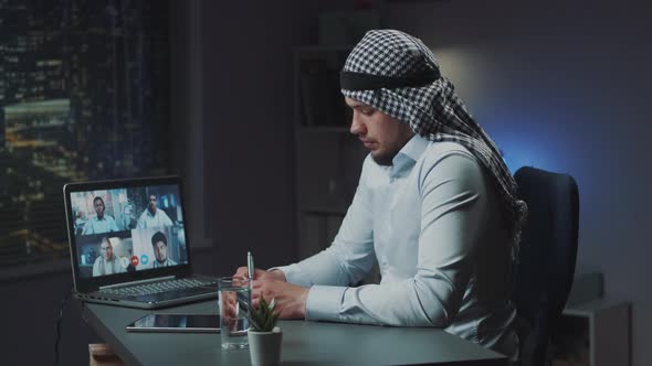 Arabic Man with Kandora Sitting at the Table and Videoconferencing with Doctors on Coronavirus alt