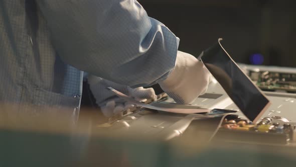 worker connects electronic circuit boards with cables at a TV factory alt