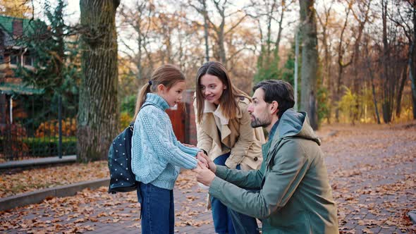 Young Parents Smiling Talking to Little Daughter Schoolgirl with Backpack alt