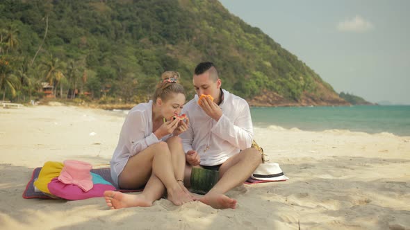 The Cheerful Love Couple Holding and Eating Slices of Watermelon on Tropical Sand Beach Sea alt