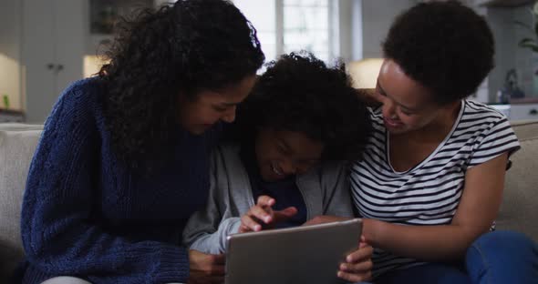 Mixed race lesbian couple and daughter using digital tablet on couch laughing alt