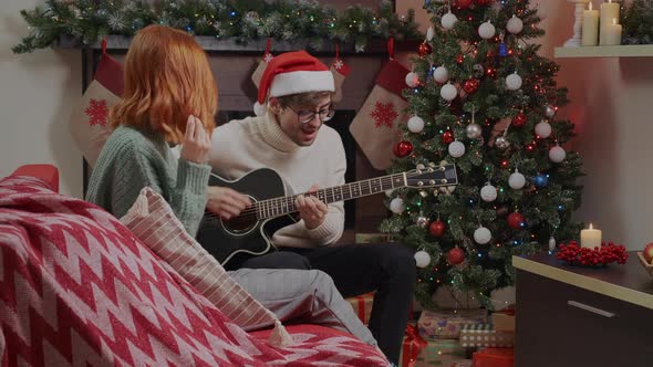 Happy couple having fun with Christmas lights next to Xmas tree at holiday evening alt
