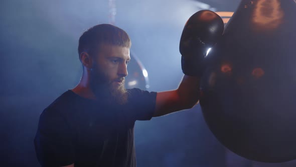 Male Boxer is Resting After Hard Training Rested His Hand on a Punching Bag on the Smoky Gym alt