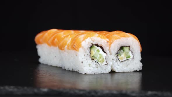 Sushi Rolls Rotate on Black Background. Close-up Shoot. Philadelphia Cheese, Cucumber and Salmon in