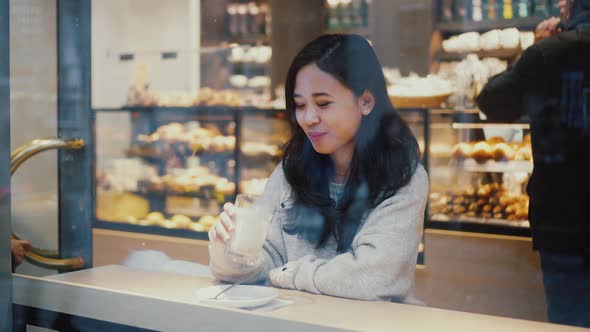 Young Asian Woman is Looking at the Street While Drinking Coffee Alone in Cafe