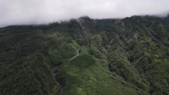 Aerial view of flying in a tropical forest, mountain, and valley in Indonesia. alt