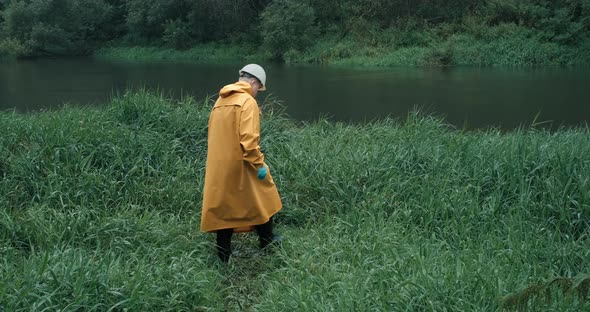 Ecologist in Raincoat Takes Sample of Water From Reservoir Into Test Tube