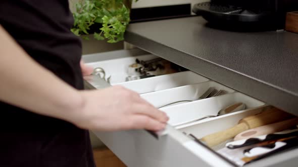 Girl or Woman in Black Tshirt and Short Shorts Walks Over to Cutlery Drawer and Picks Up Two Shiny alt
