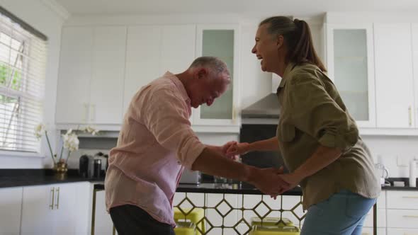 Caucasian senior couple dancing together in the kitchen at home alt