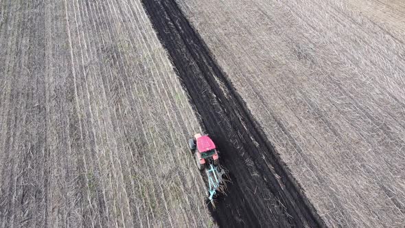 Shooting From Drone Flying Over Tractor with Harrow System Plowing Ground on Cultivated Farm Field