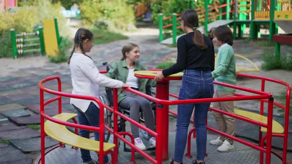Group of Caucasian Children Enjoying Leisure on Playground with Friend in Wheelchair alt