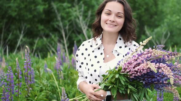 Young Beautiful Woman Posing in a Field with a Bouquet of Lilac Flowers. Happy Brunette in a Field alt