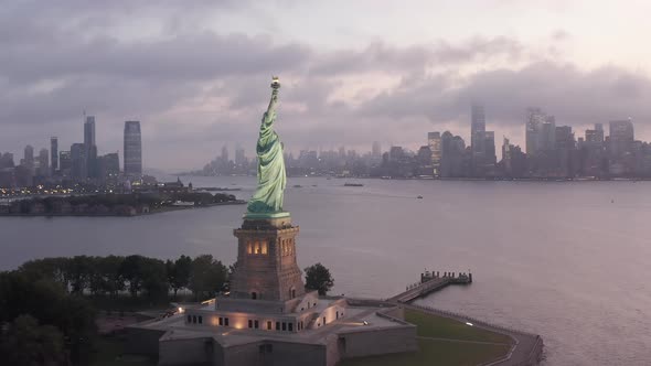 Circling Statue of Liberty Illuminated in Early Morning Light with Foggy New York City alt